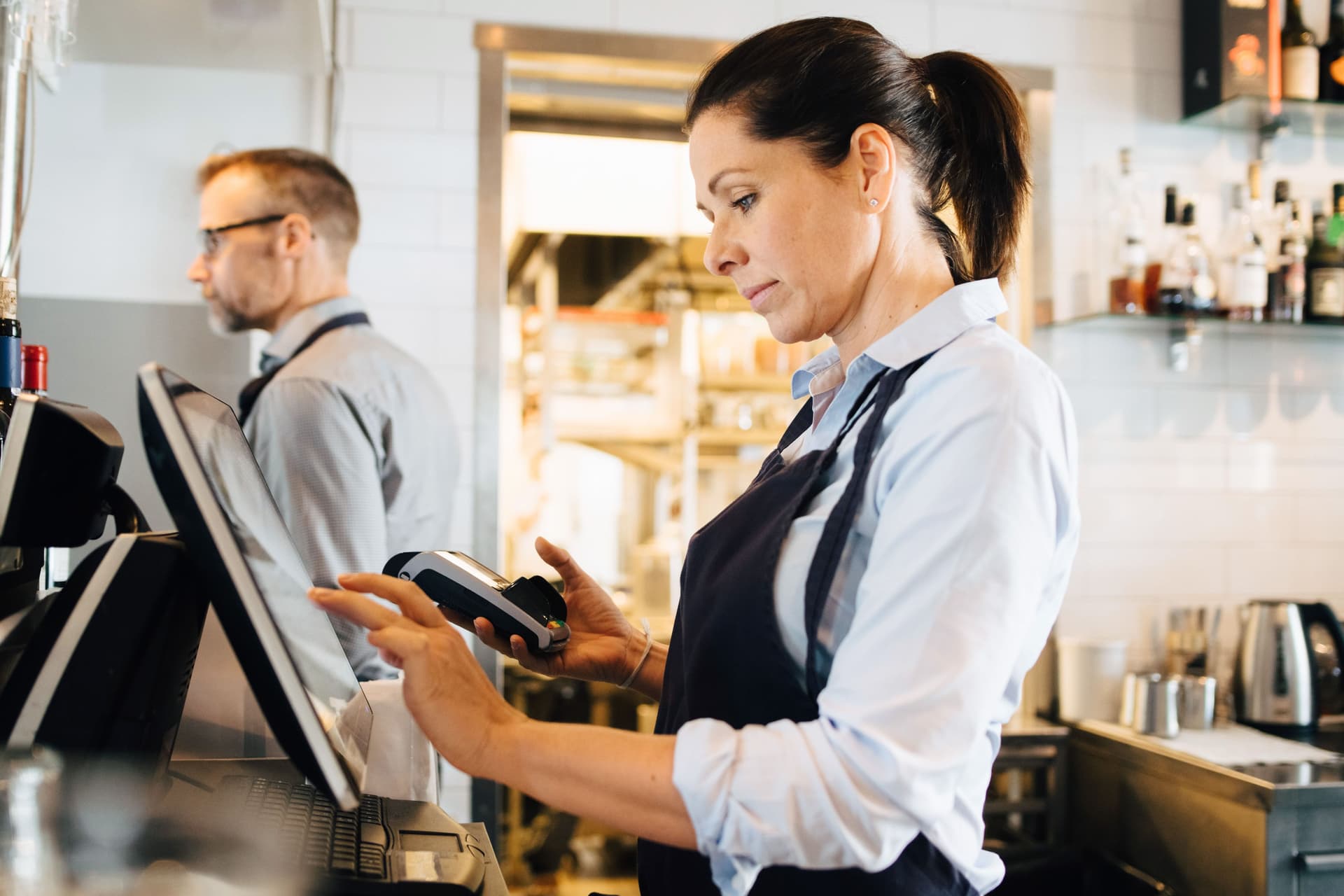 Besitzer, der Computer benutzt, während er Kreditkartenleser im Restaurant hält