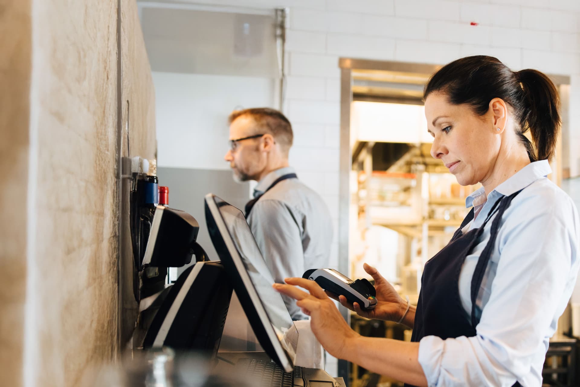 Mitarbeiterin in der Gastronomie hält ein Kartenlesegerät in der Hand und tippt auf einem Bildschirm
