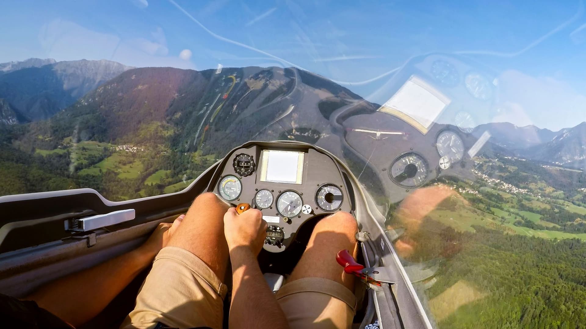 Blick auf begrünte Berge und einen blauen Himmel aus einem Segelflugzeug.