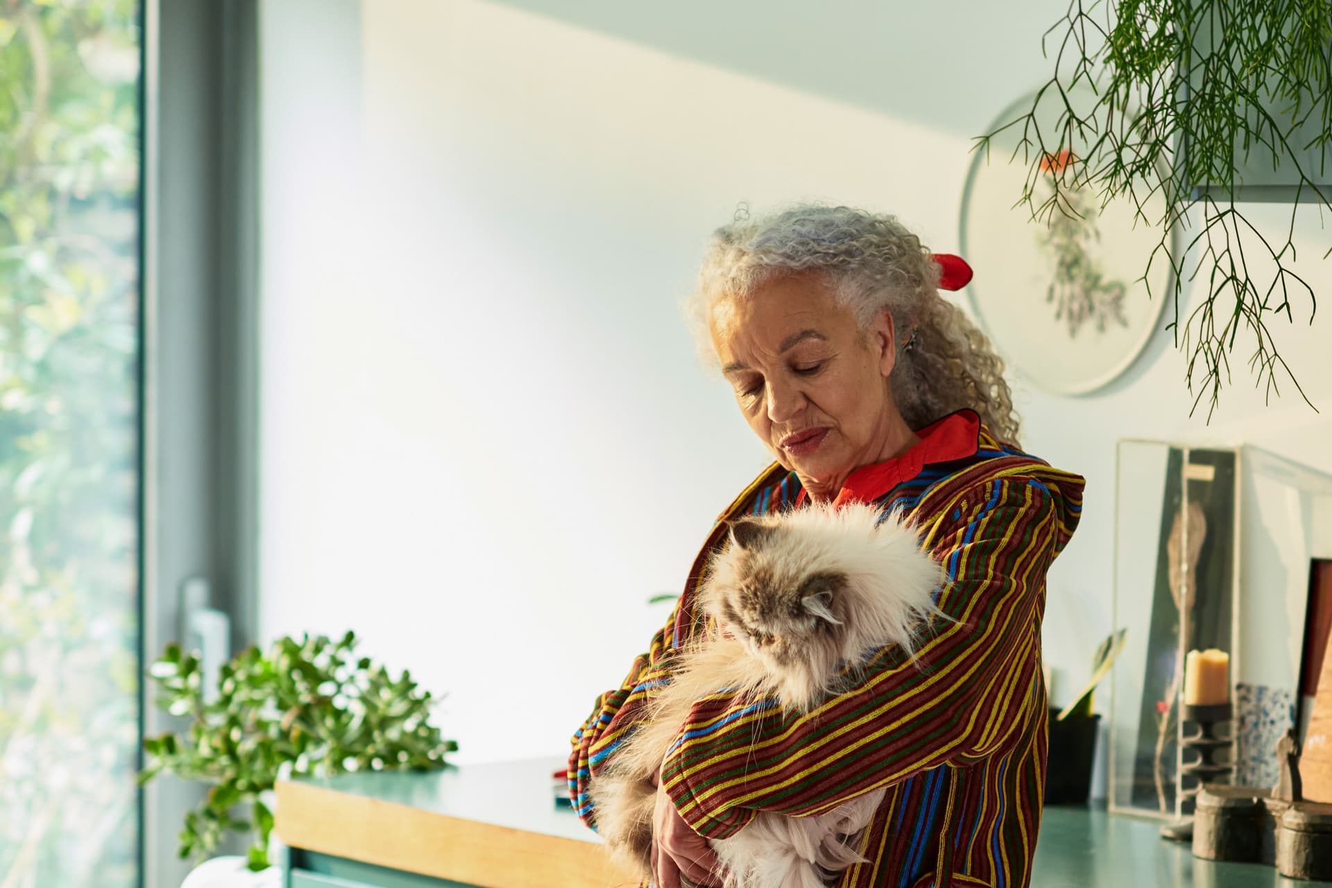 Seniorin lehnt an einer Küchenzeile und hält eine Katze auf dem Arm.