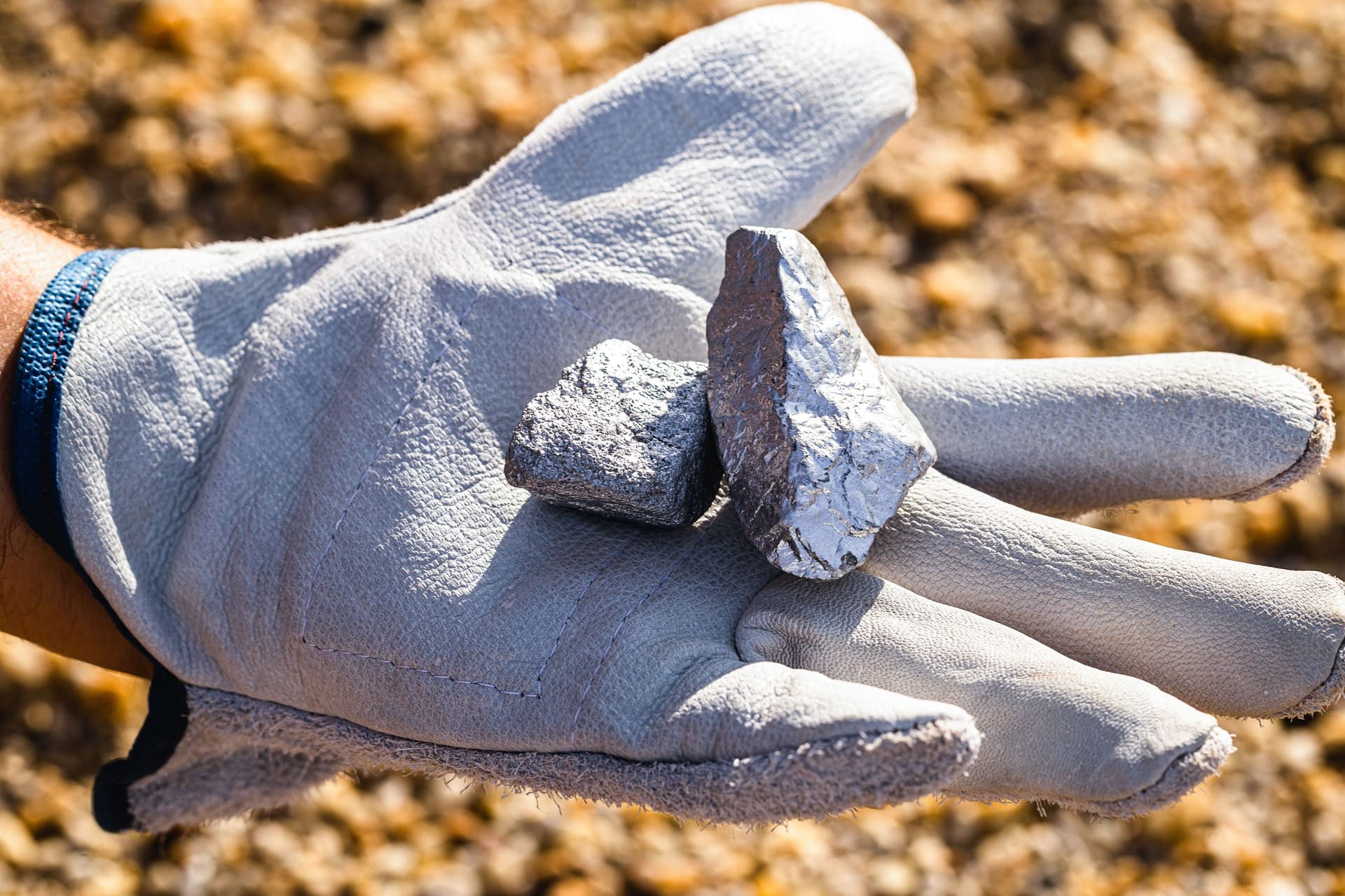 Hand mit einem weißen Handschuh, die Silbersteine und Silbererz hält.