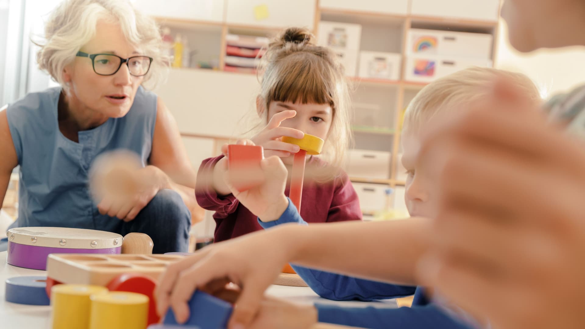 Kinder und Erzieherin im Kindergarten. Sie spielen zusammen mit Musikinstrumenten an einem Tisch.