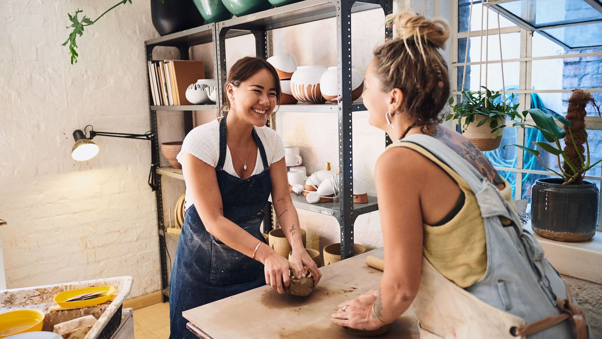 Aufnahme von zwei jungen lächelnden Frauen, die Ton in einem Töpferatelier kneten.