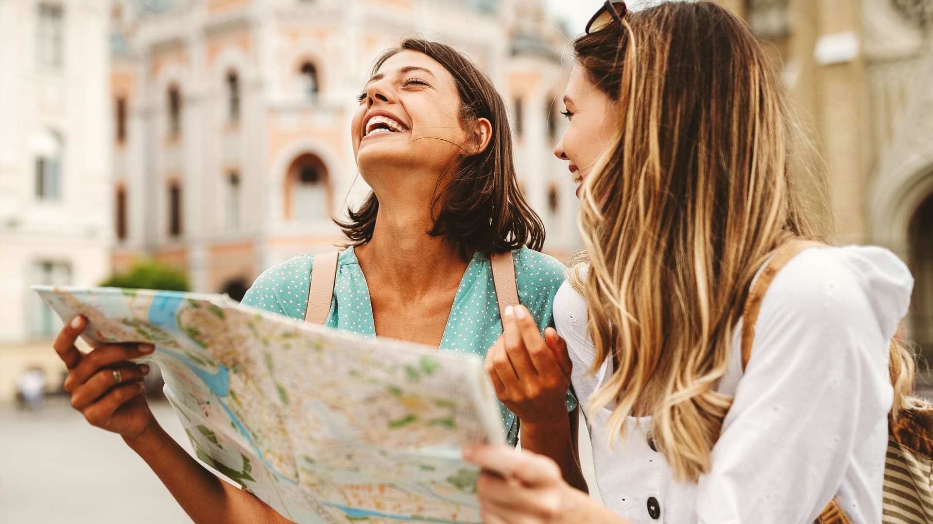 Lachende Touristinnen mit Stadtplan in einer Stadt.