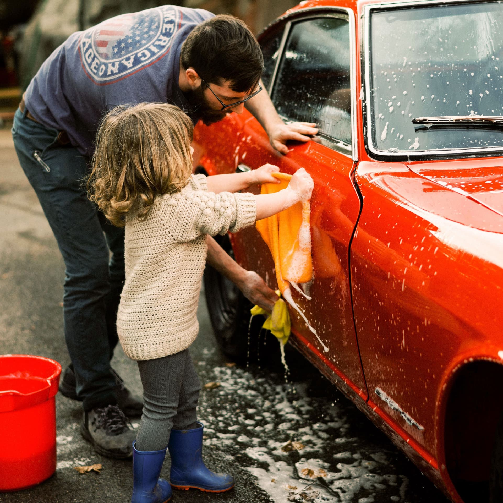 Tochter und Vater reinigen zusammen einen roten Oldtimer.