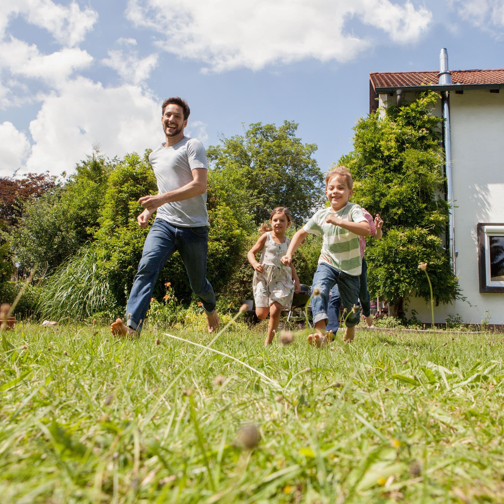 Ein Vater mit Sohn und Tochter rennt im Garten eines Hauses.