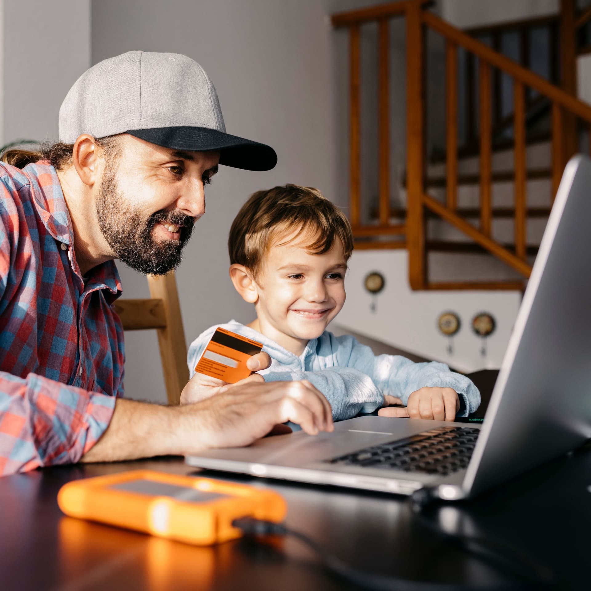 Mann und Kind sitzen am Laptop. Mann hält eine Kreditkarte in der Hand.