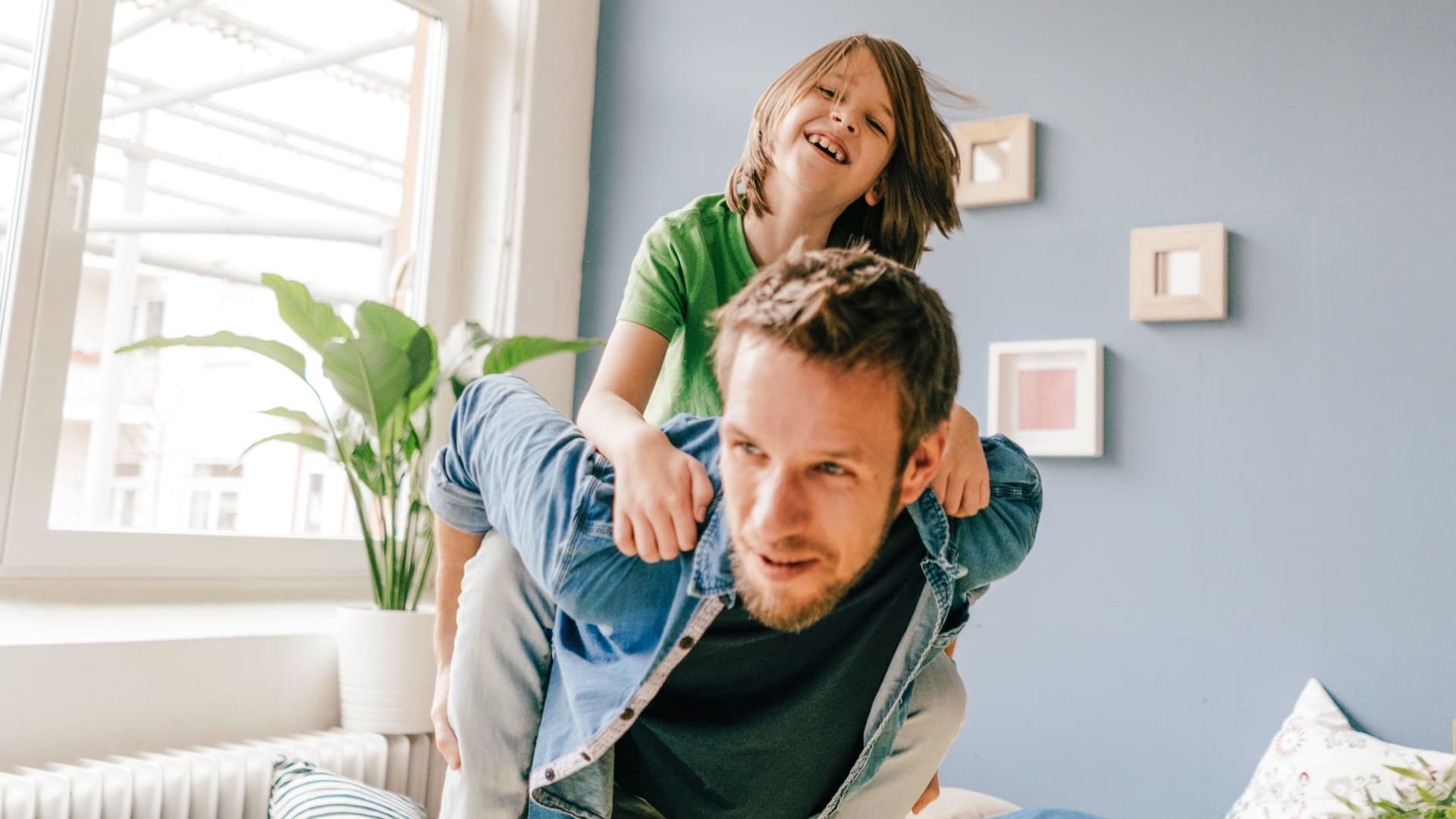 Lachendes Kind wird vom Vater in der Wohnung Huckepack getragen.