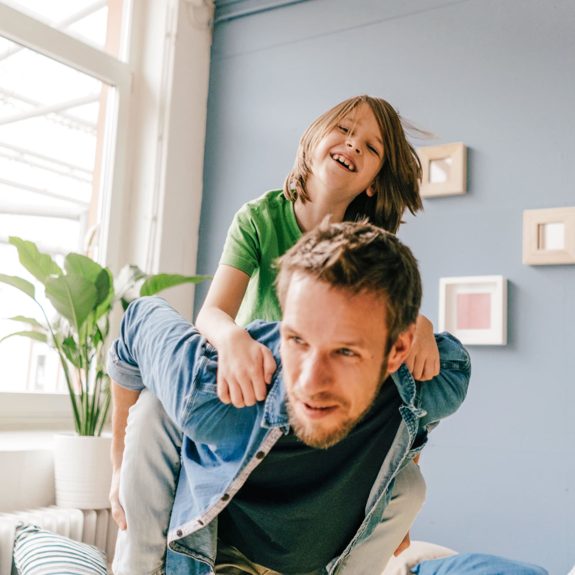 Lachendes Kind wird vom Vater in der Wohnung Huckepack getragen.