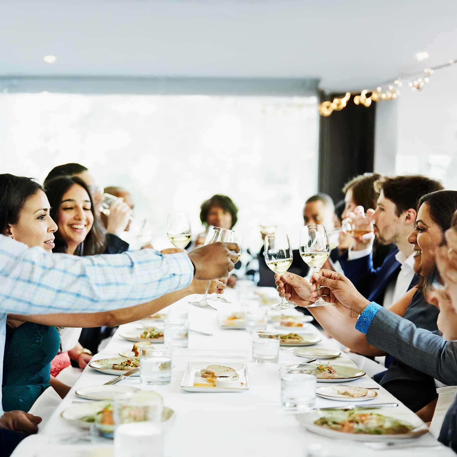 Viele Menschen sitzen an einem langen Tisch in einem Restaurant und stoßen mit Weingläsern an