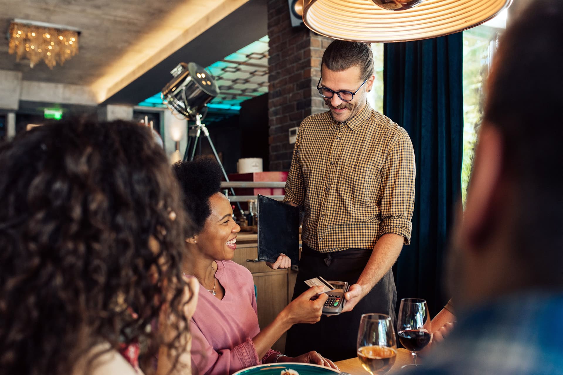 Eine Businessfrau zahlt im Restaurant mit ihrer Visa-Business-Card beim Kellner die Rechnung für ein Geschäftsessen mit mehreren Kollegen.
