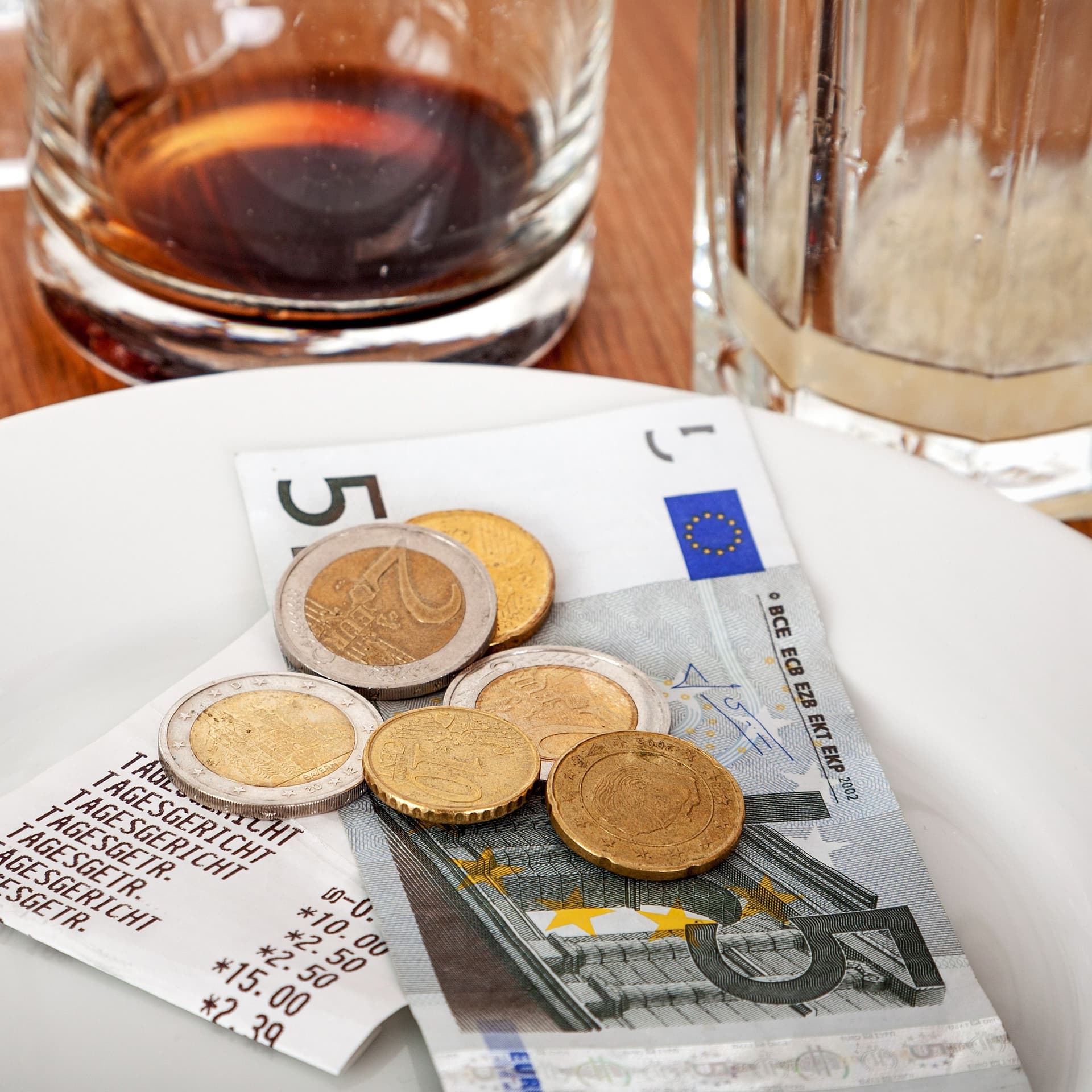 Leere Gläser auf einem Tisch. Bargeld liegt mit Beleg auf einem Teller daneben.