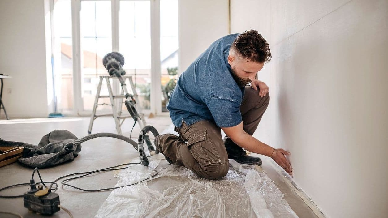 Ein Handwerker schleift auf einer Baustelle eines Privathauses eine Trockenbauwand. 


