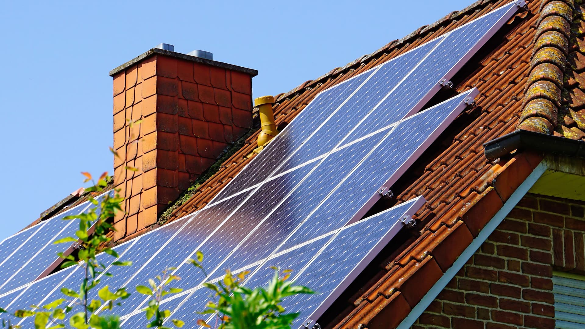 Von einem Einfamilienhaus ist nur das Dach und ein Schornstein zu sehen. Auf der Dachschräge sind eine Vielzahl von Solarpannels zu sehen.