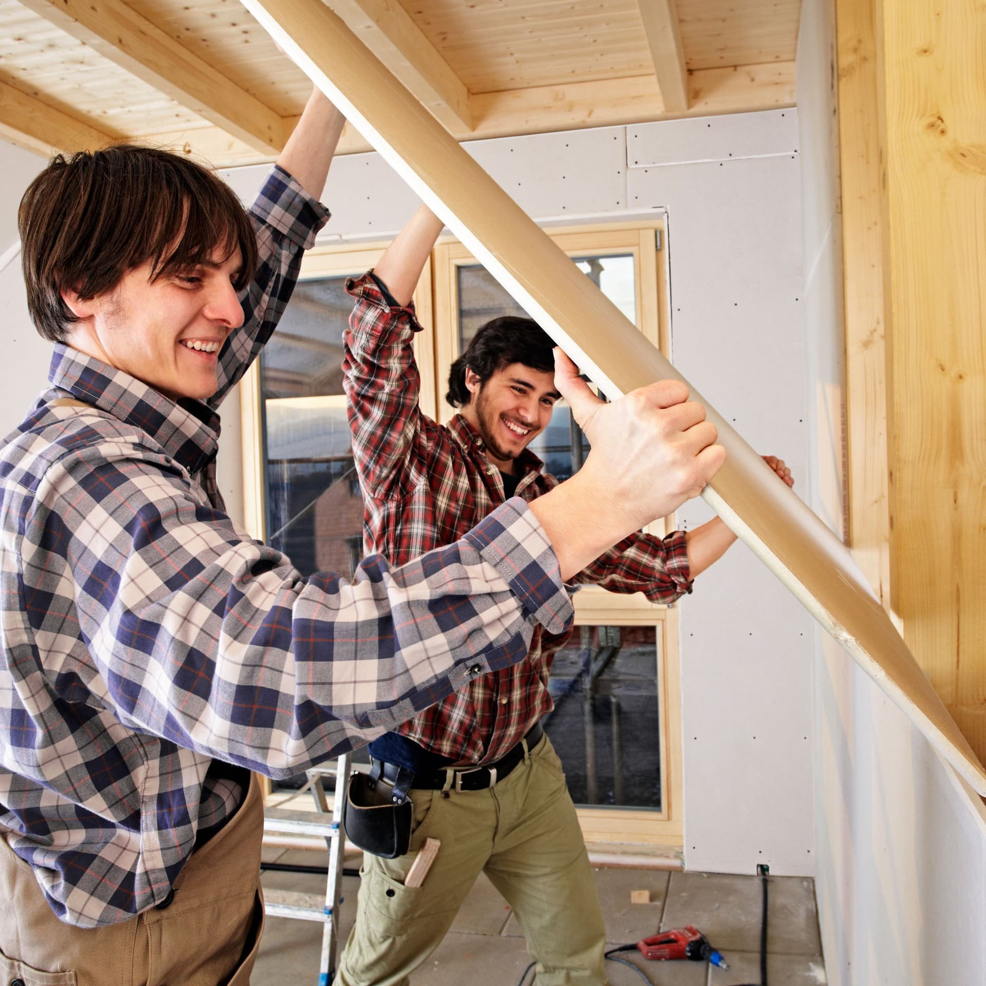 Zwei Männer in Holzfällerhemden, die einen Holzbalken befestigen.