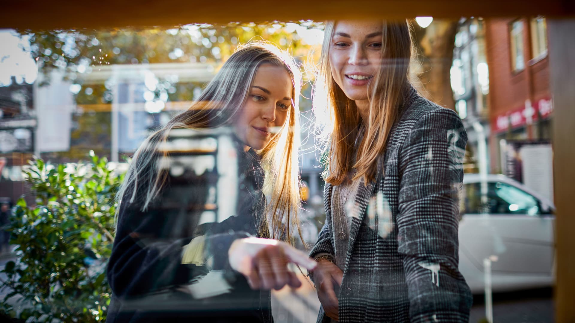 Blick von Innen durch ein Schaufenster auf zwei junge Frauen, die davor stehen und hindurchschauen. Eine der beiden zeigt auf die Auslage.
