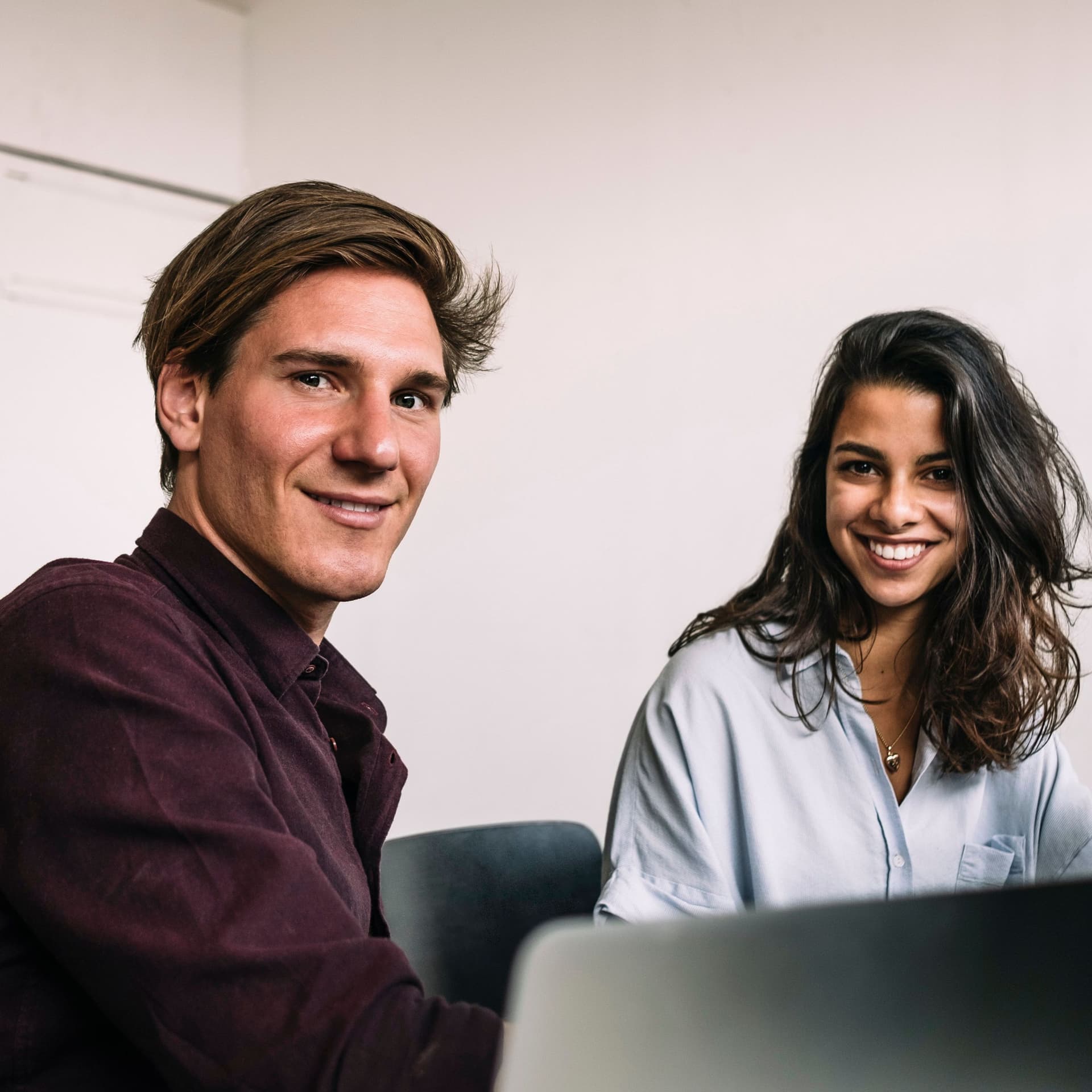 Porträt zweier Studenten, die vor einem Computer sitzen und lächelnd in die Kamera schauen.