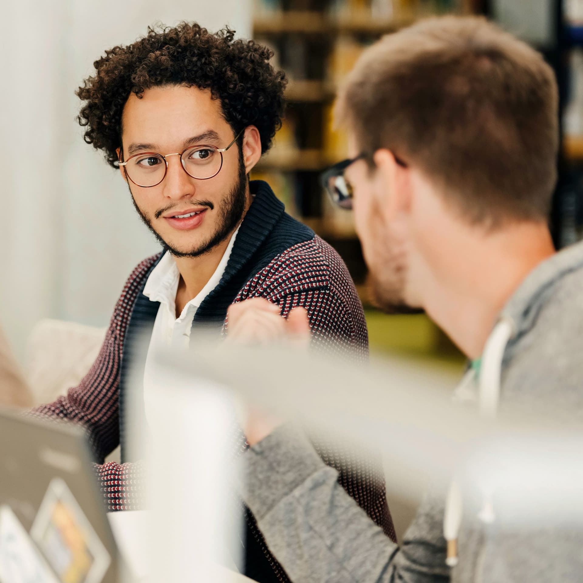 Zwei Studenten vor ihren Laptops, die sich beim Lernen in der Bibliothek leise unterhalten.