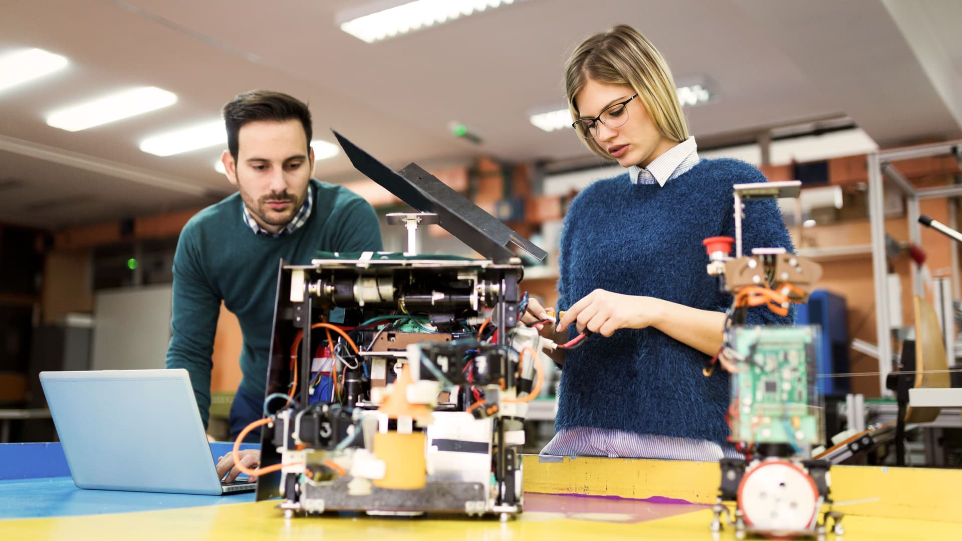 Eine Frau und ein Mann arbeiten gemeinsam an einem Robotik-Projekt vor ihnen auf dem Tisch.