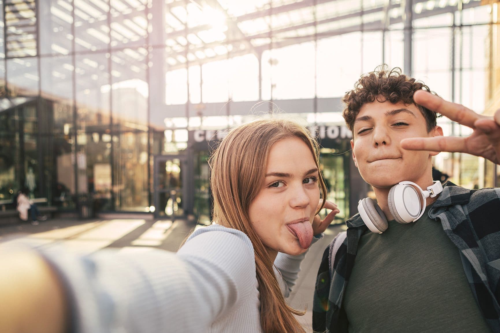 Zwei Jugendliche machen mit einem Smartphone ein Selfie vor einem Glasgebäude.