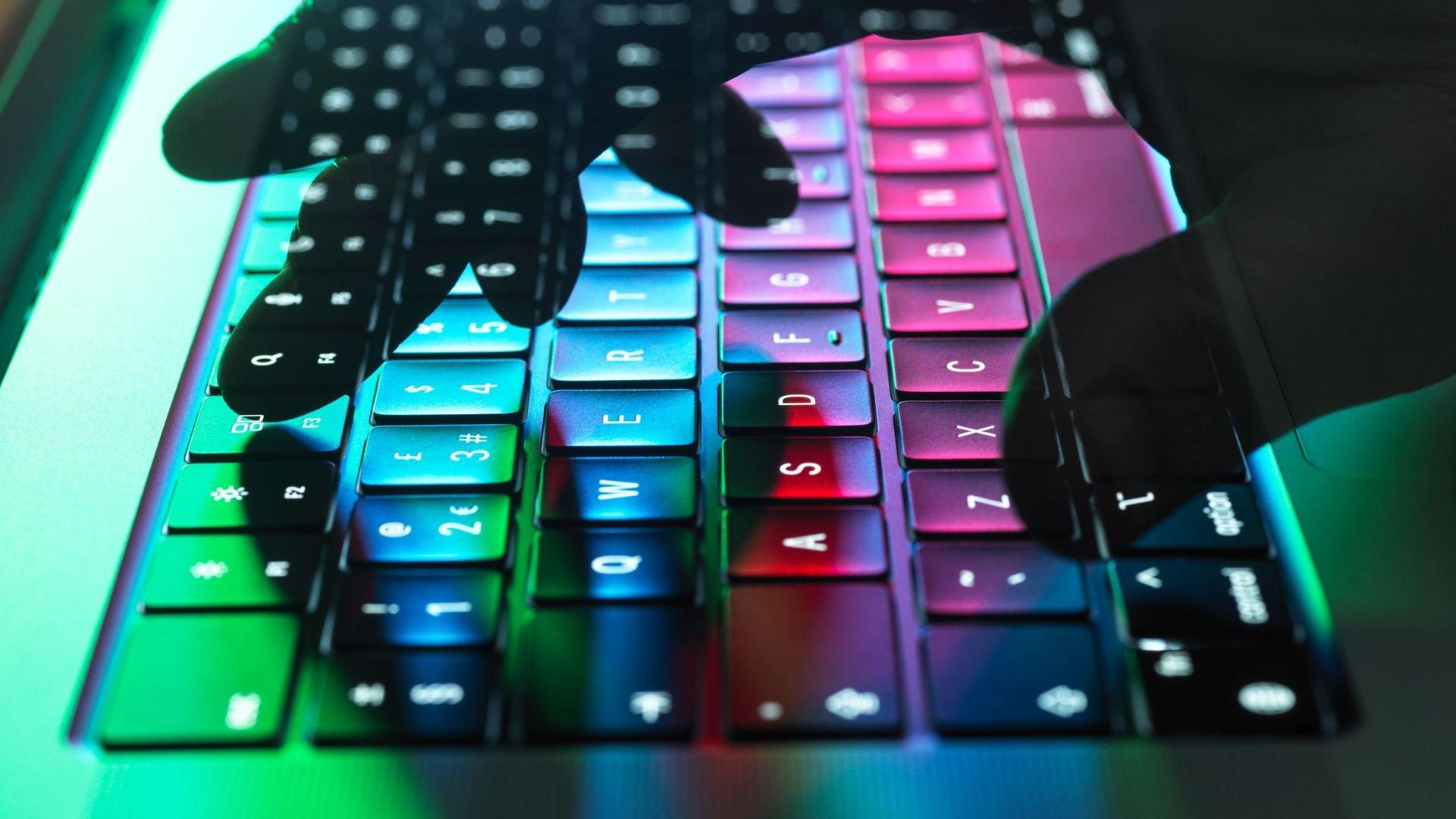 Eine Hand tippt auf einer Tastatur, welche in Regenbogenfarben leuchtet.