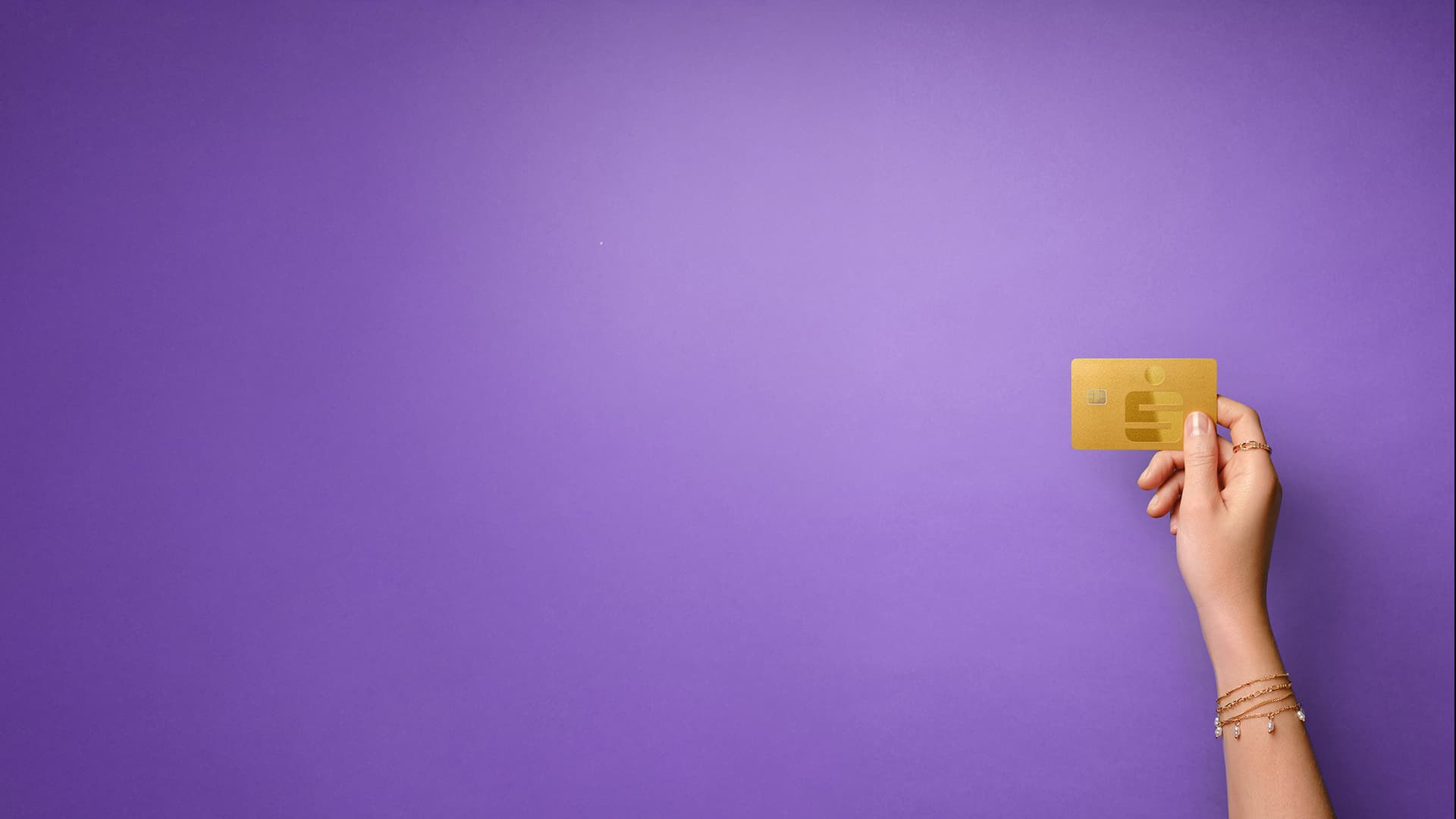 Eine Hand hält eine goldene Sparkassen-Karte vor violettem Hintergrund.