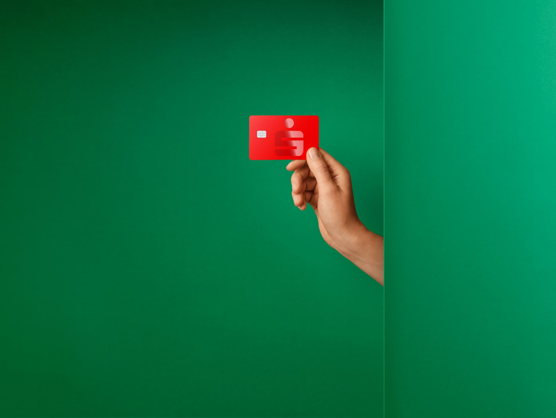 Hand hält eine rote Sparkassen-Kreditkarte vor grünem Hintergrund