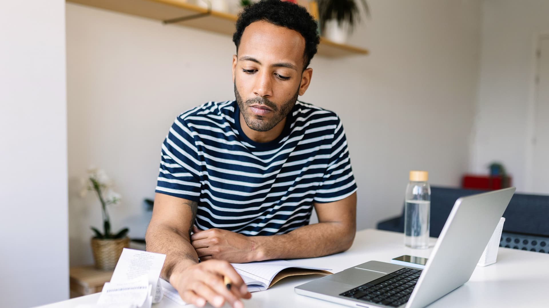Ein junger Mann sitzt an einem Schreibtisch und rechnet mit einem Taschenrechner