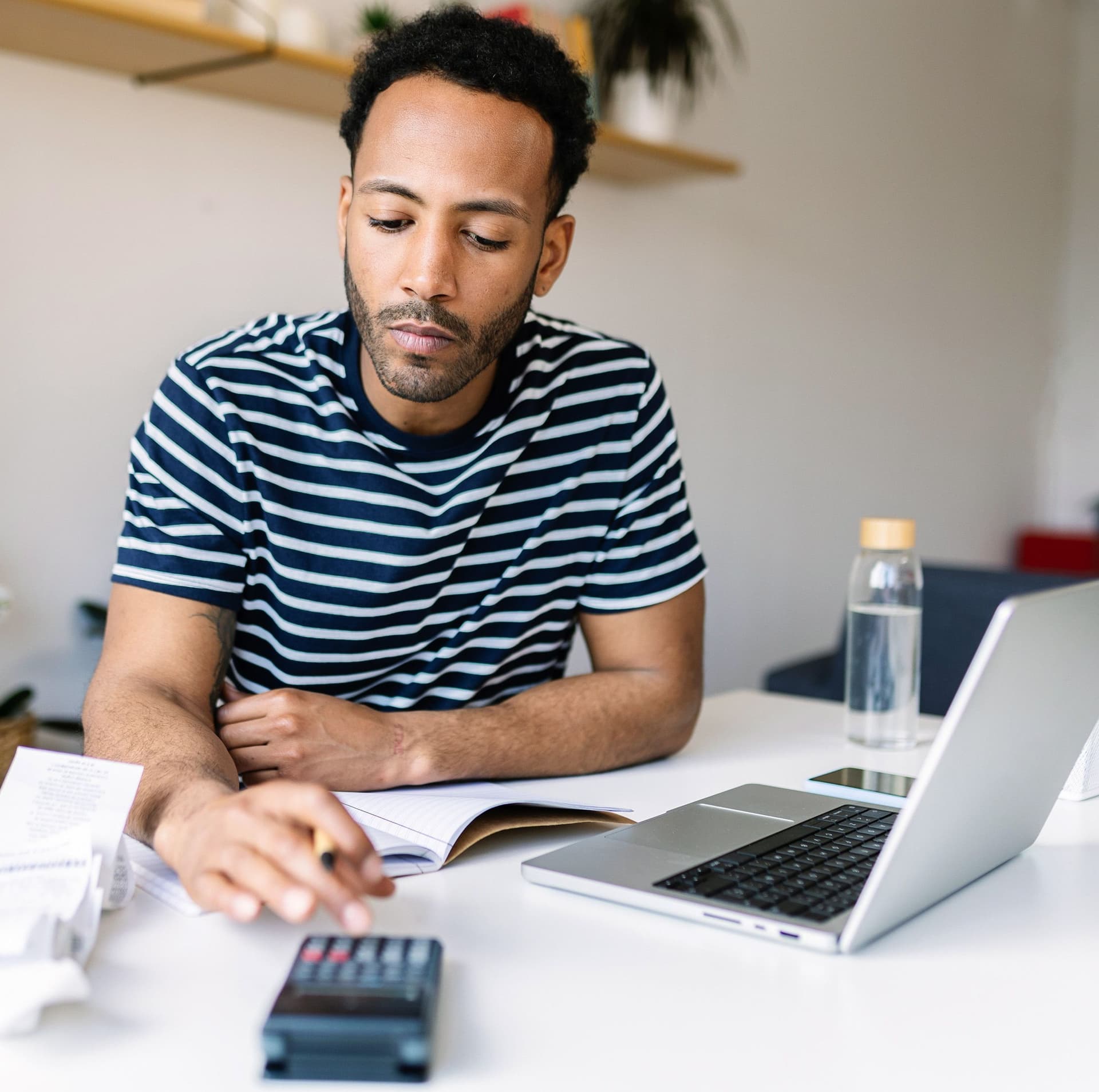 Ein junger Mann sitzt an einem Schreibtisch und rechnet mit einem Taschenrechner
