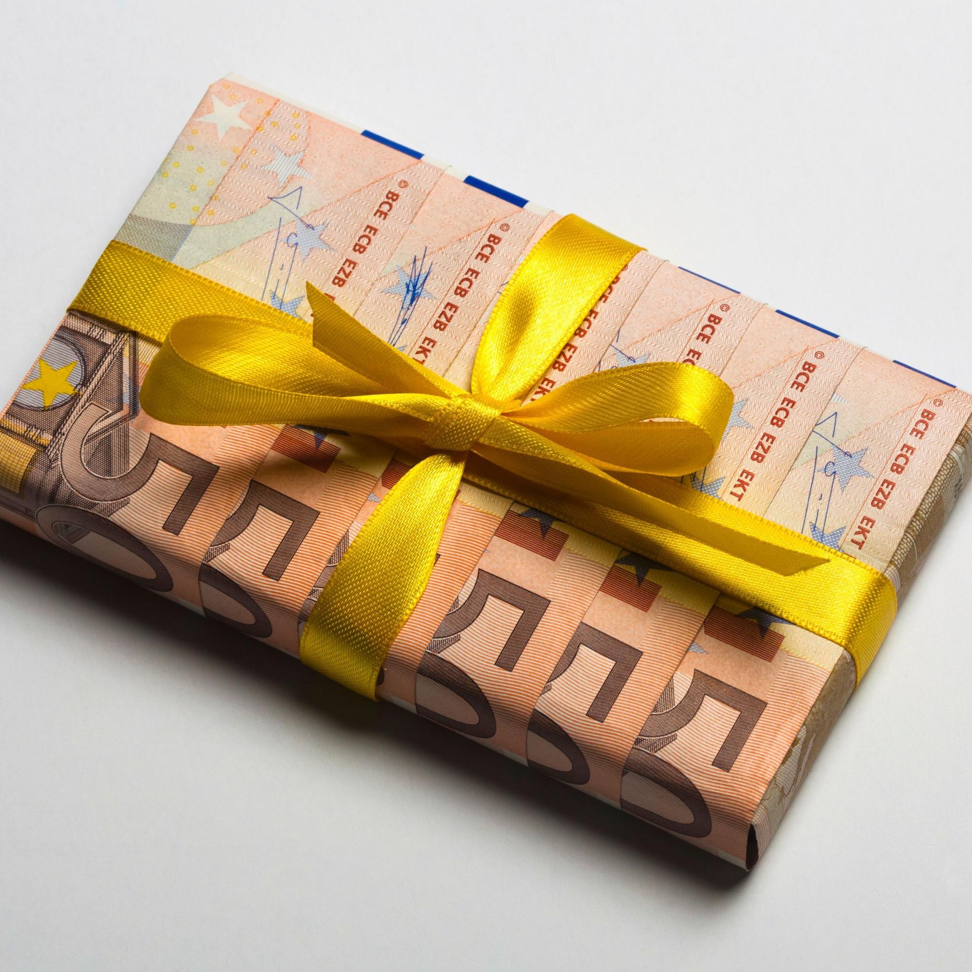 Fünfzig Euro-Geldscheine, die gefaltet wurden, um ein Geschenk damit zu verpacken. Darum ist eine gelbe Schleife aus Geschenkband.