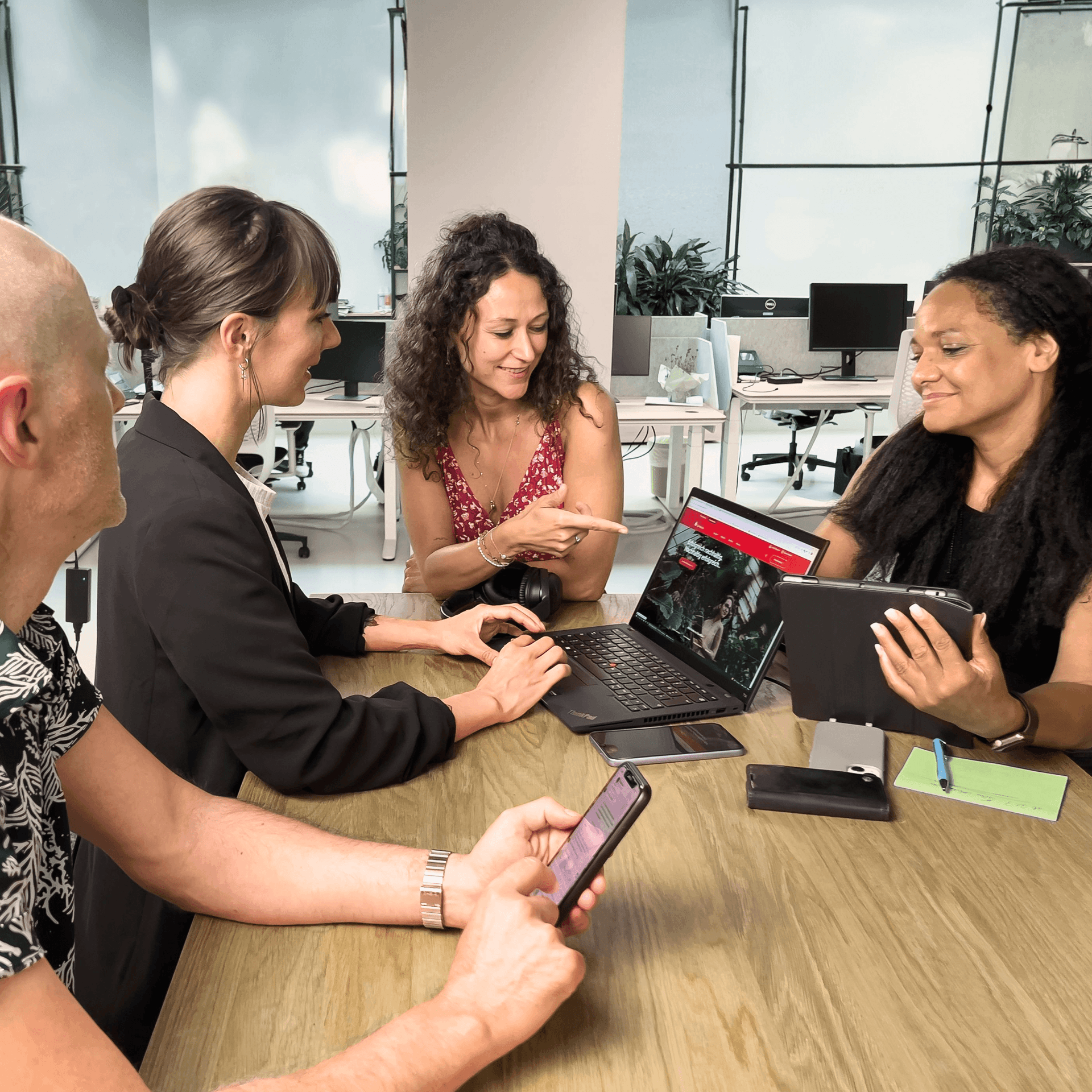 Drei Frauen und ein Mann sitzen an einem Konferenztisch im Büro an einem Laptop und haben eine Besprechung.