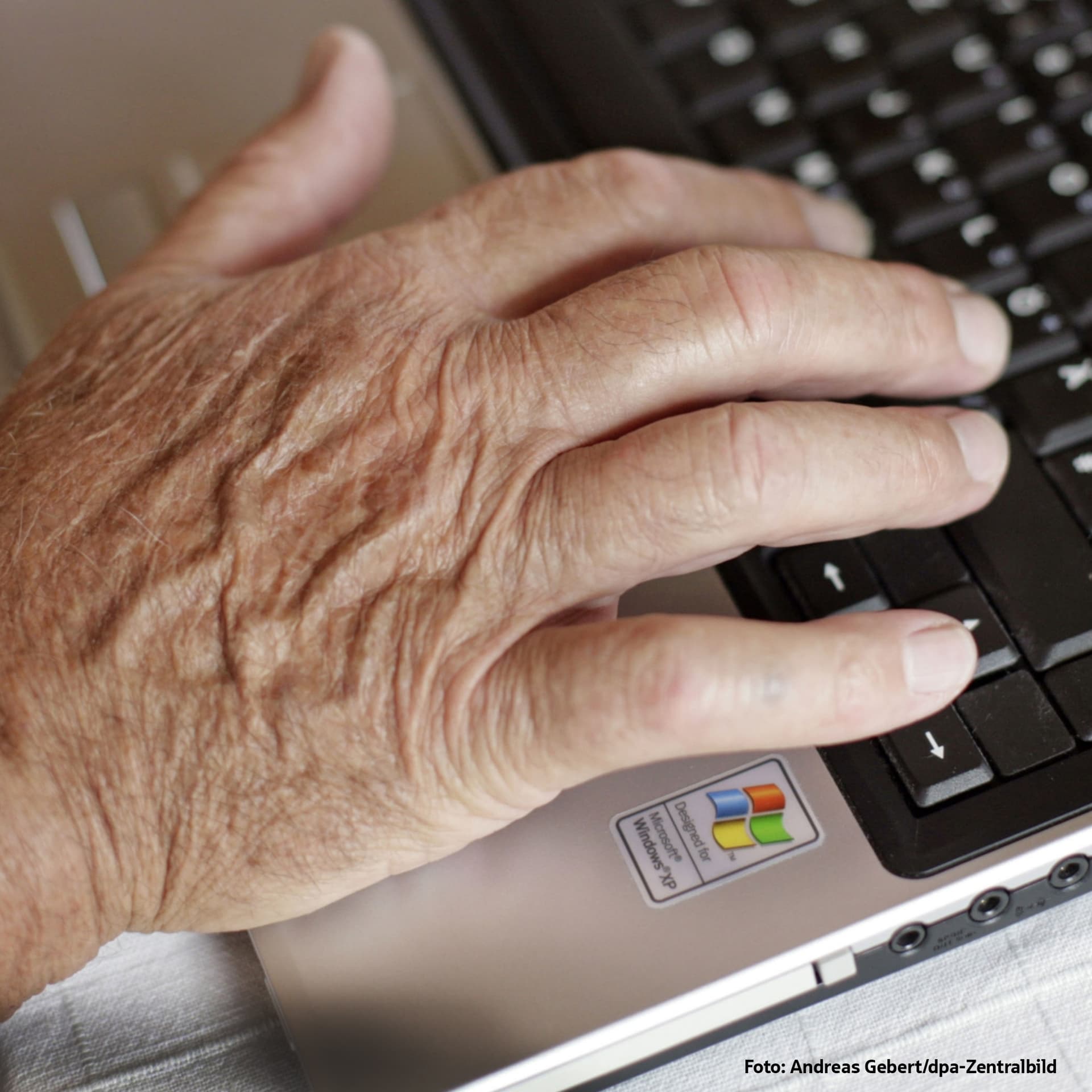Hand einer älteren Person auf Laptop-Tastatur