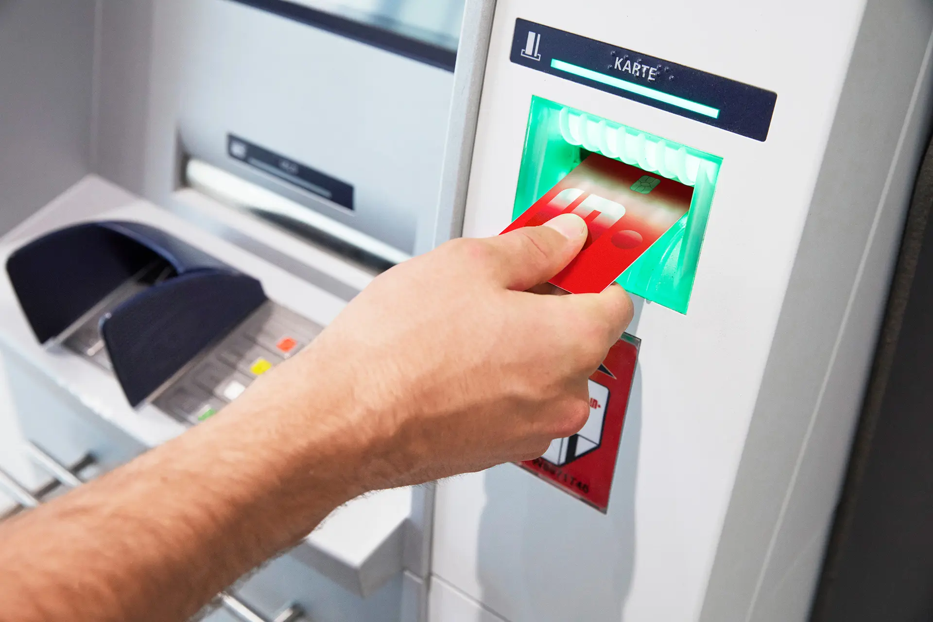 Hand steckt eine rote Sparkasse Debitkarte in den Kartenschlitz eines Geldautomaten.