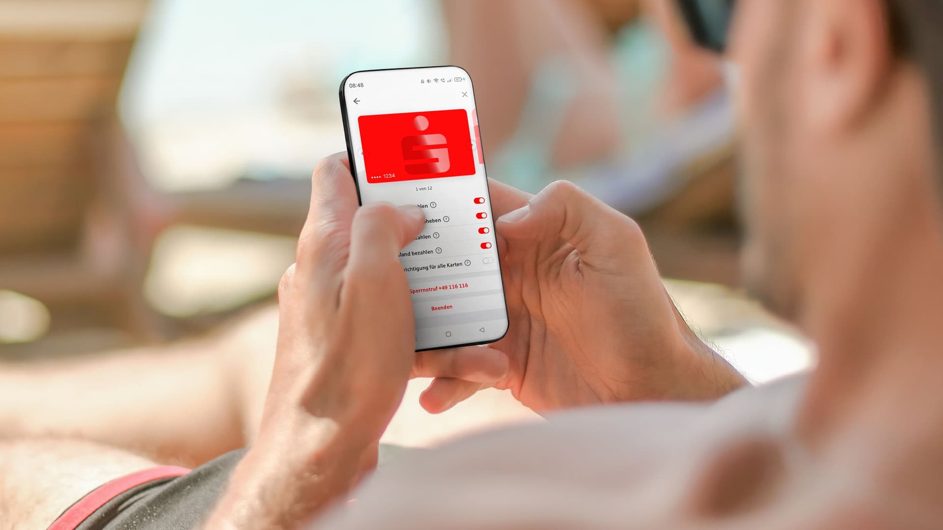 Jemand hält ein Smartphone mit der Sparkasse Card Control App. Die App zeigt eine rote Karte und Schalter, um Funktionen wie Bezahlen und Abheben der Karte ein- oder auszuschalten.