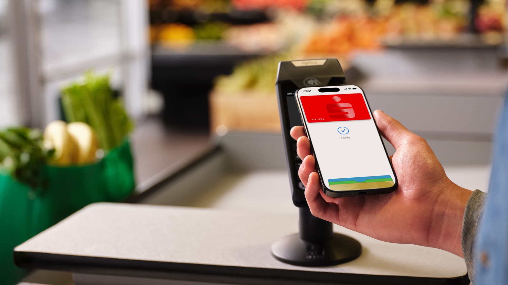 Eine Hand hält ein Smartphone mit einer Sparkassen-Karte in einer Supermarktkasse, bereit für eine kontaktlose Zahlung.