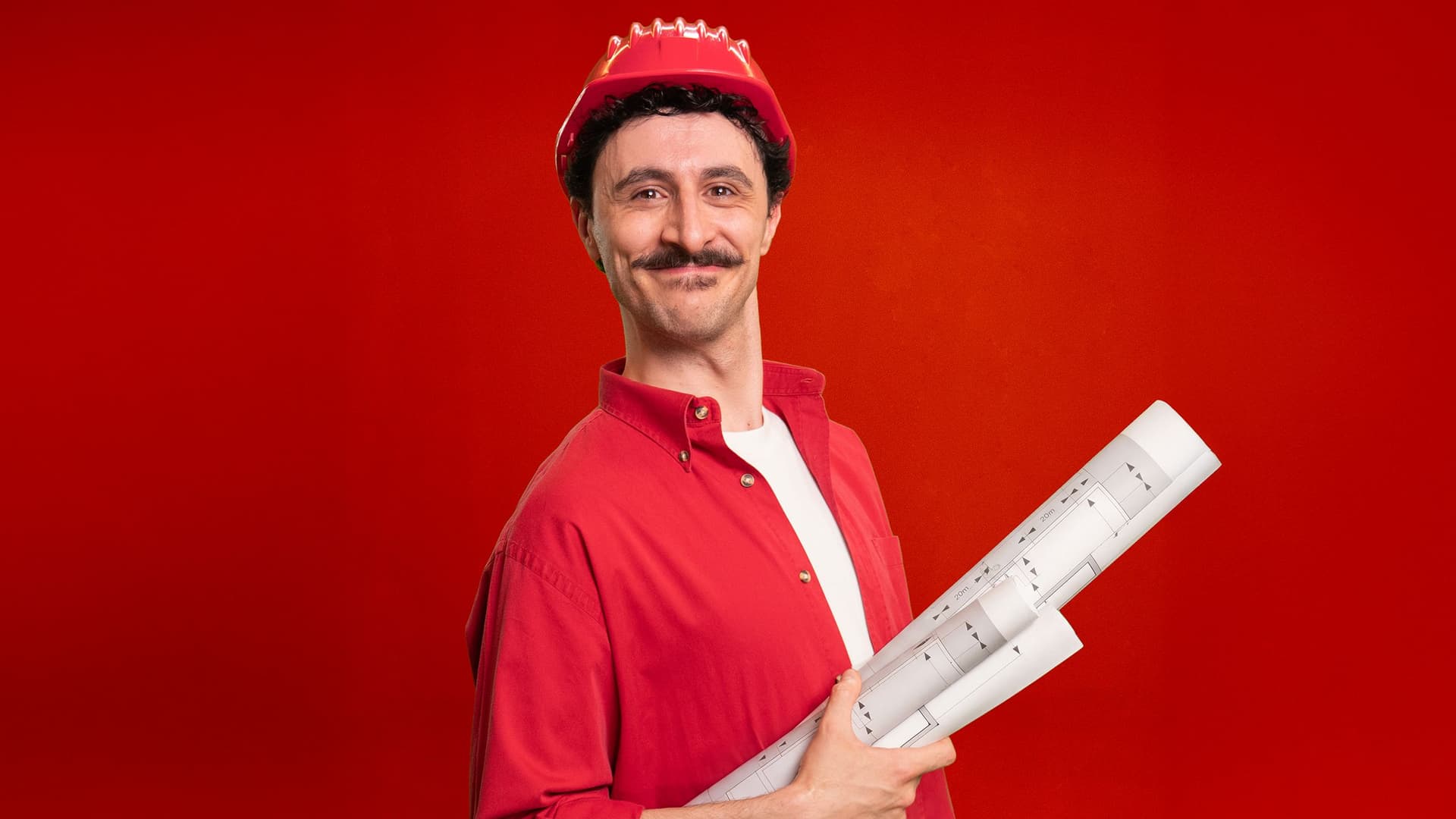 Mann mit roten Hemd und Bauhelm, hält Baupläne vor rotem Hintergrund.