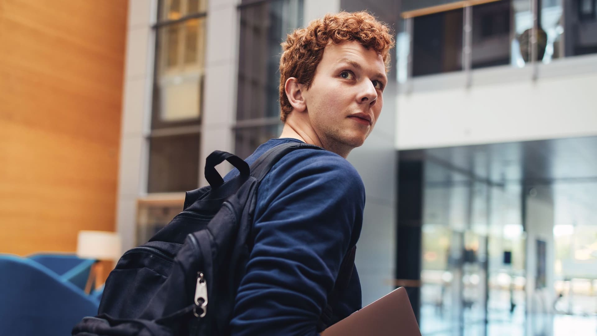 Student mit Laptop unterm Arm blickt über seine Schulter Richtung Kamera.