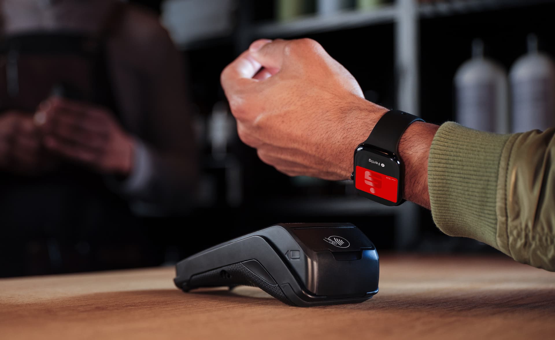 Eine Person zahlt kontaktlos mit einer Smartwatch, die eine Sparkassen-Karte anzeigt, an einem Bezahlterminal.