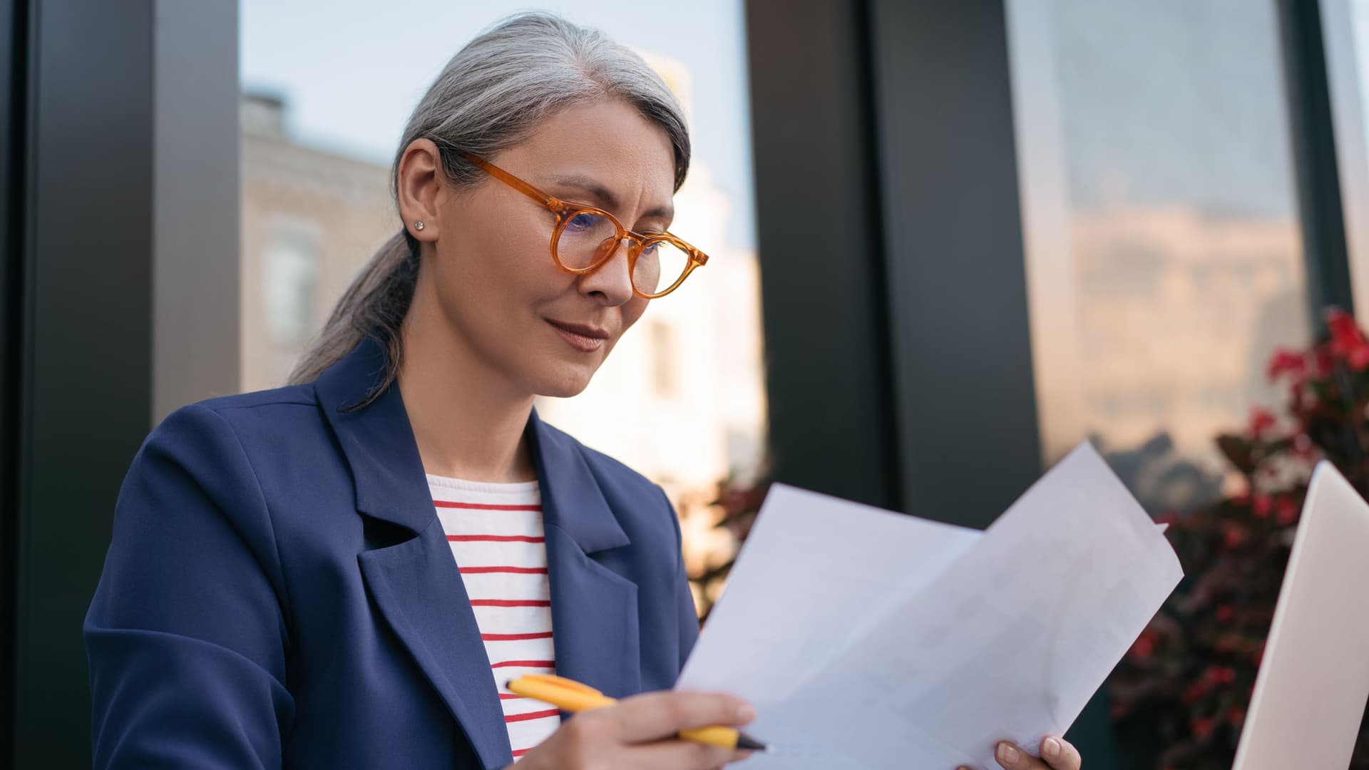 Ältere Frau amLaptop schaut sich Papiere an.