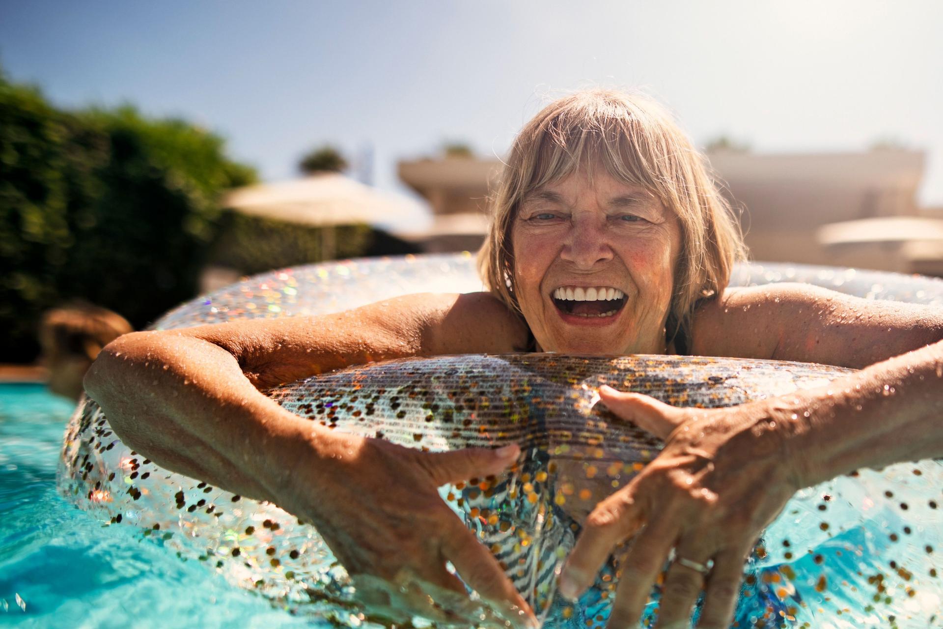 Lachende ältere Frau, die mit einem Schwimmreif in einem Swimmingpool schwimmt.