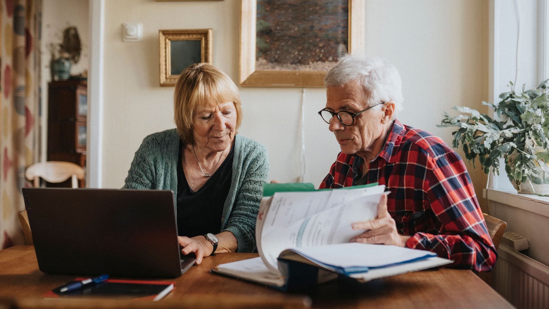 Ältere Frau und älterer Mann sitzen am isch und gehen unterlagen durch.