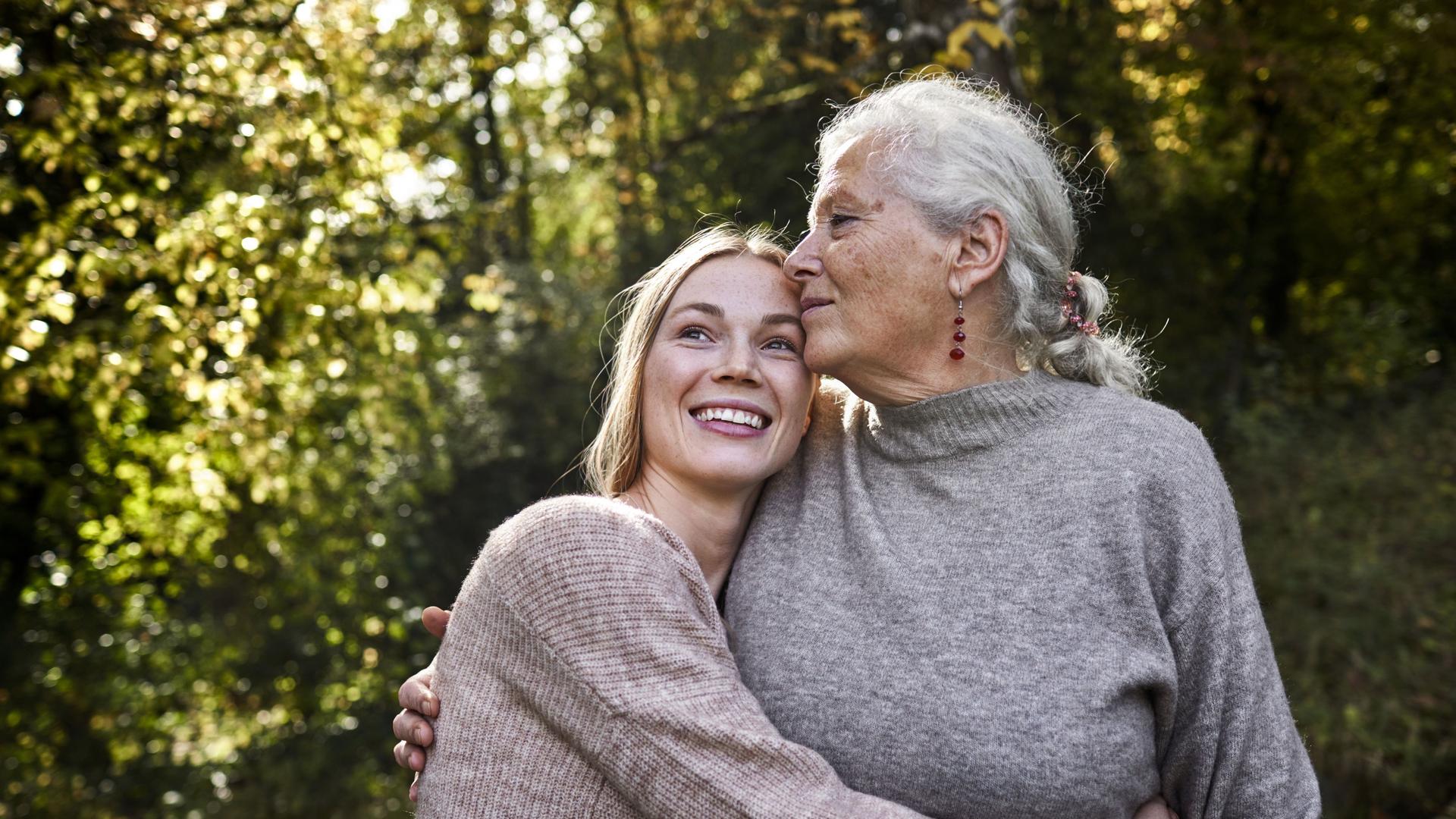 Großmutter und erwachsene Enkelin umarmen sich im Garten