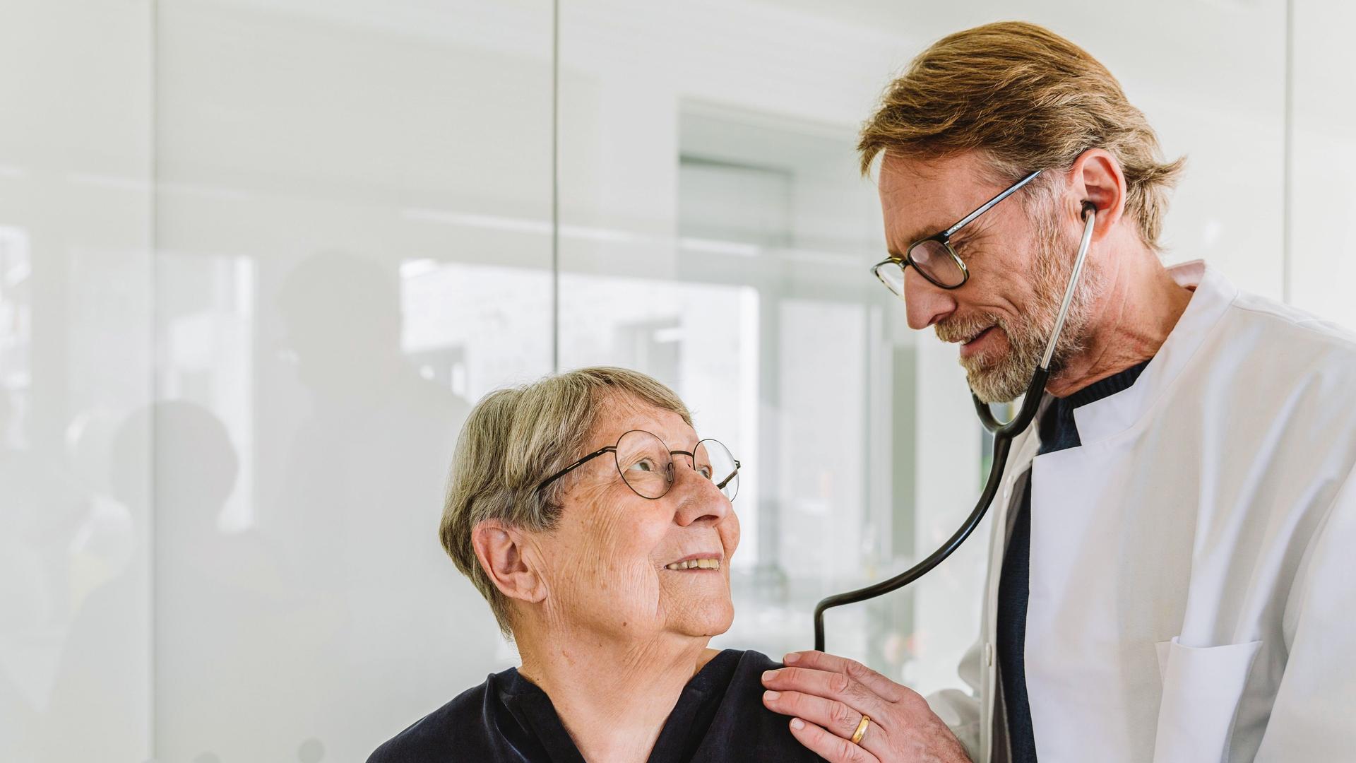 Ein Arzt untersucht eine ältere Patientin mit einem Stethoskop.