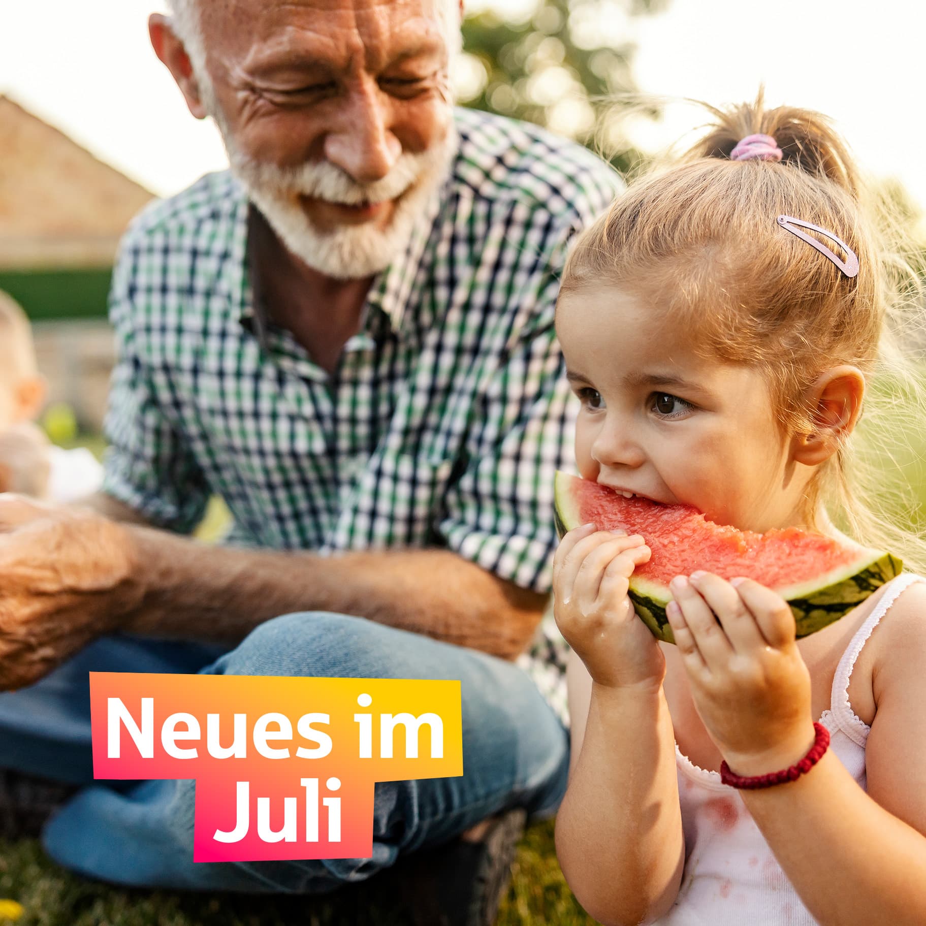 Ein älterer Mann sitzt mit zwei Kindern auf einer Wiese und isst Melone.