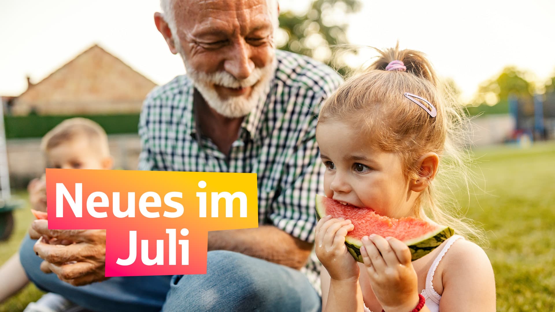 Ein älterer Mann sitzt mit zwei Kindern auf einer Wiese und isst Melone.