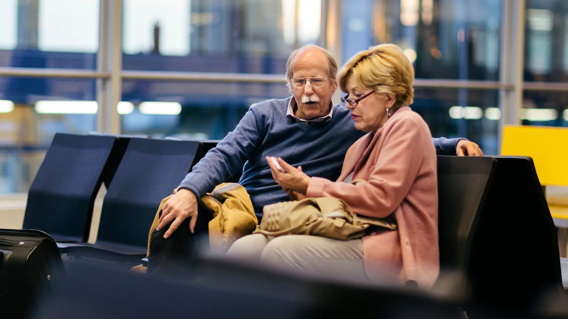 Ein älteres Paar benutzt ein Smartphone, während es am Flughafen wartet