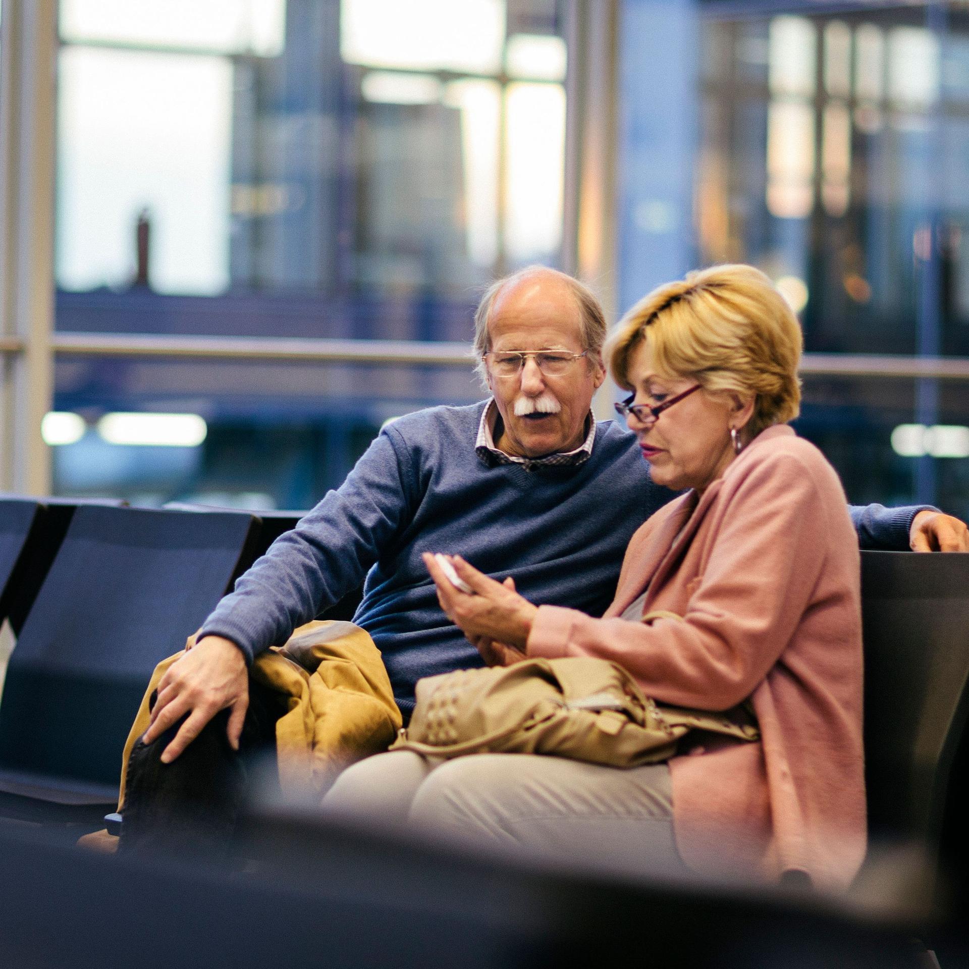 Ein älteres Paar benutzt ein Smartphone, während es am Flughafen wartet
