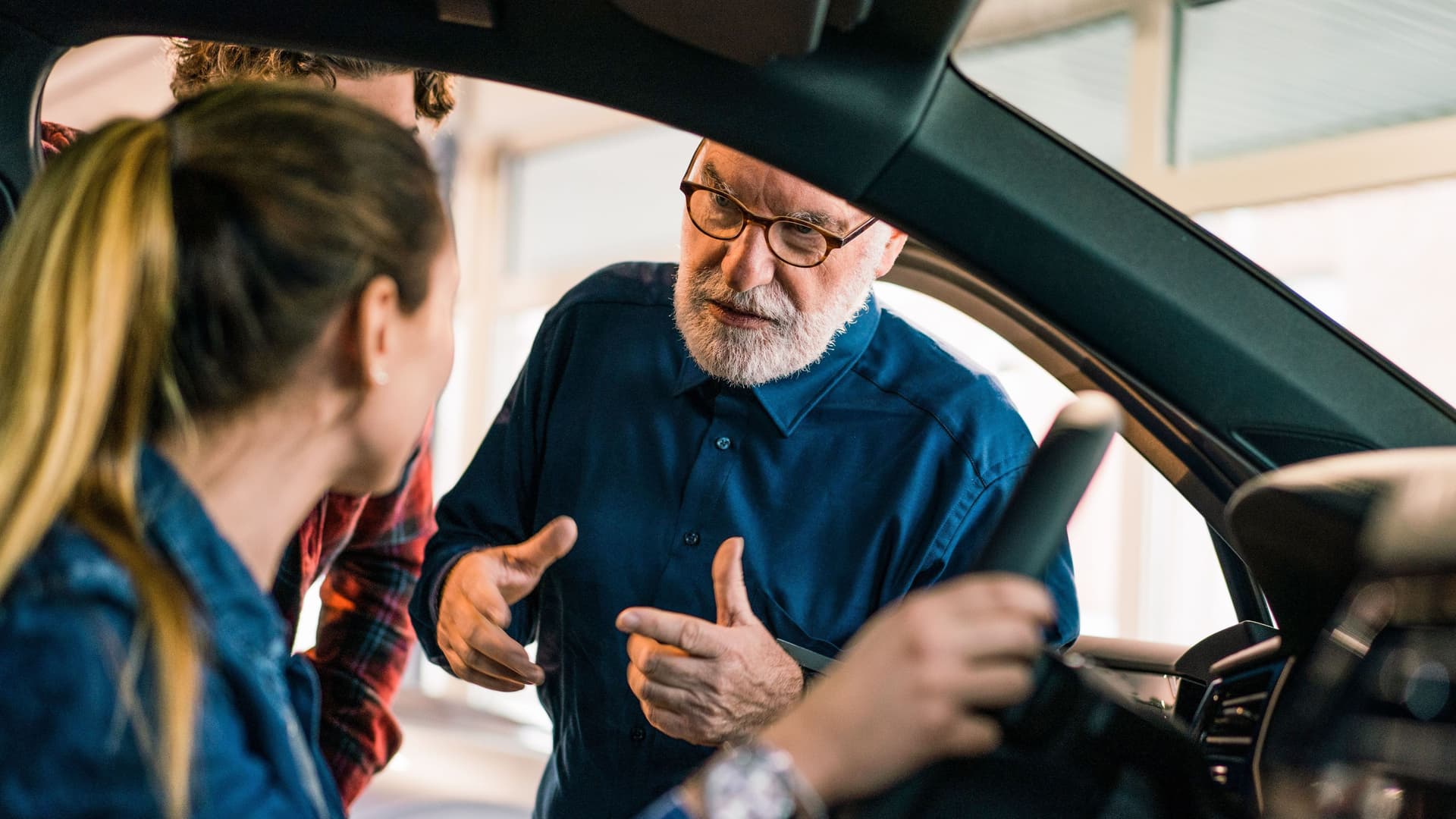 Ein Automechaniker spricht mit einer Frau, die am Steuer sitzt und erklärt ihr etwas.