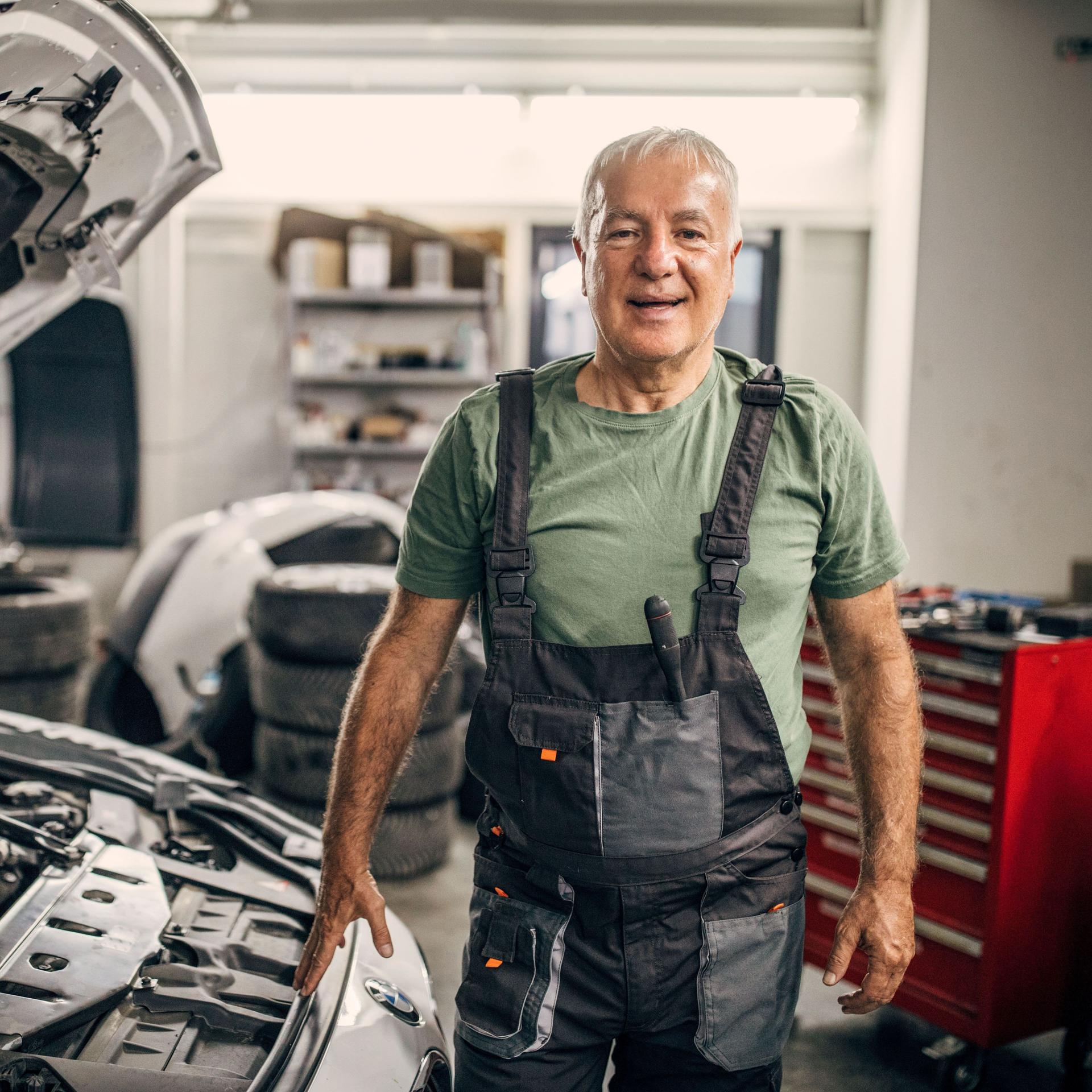 Porträt eines älteren Mannes, der in einer Autowerkstatt arbeitet und in die Kamera schaut.