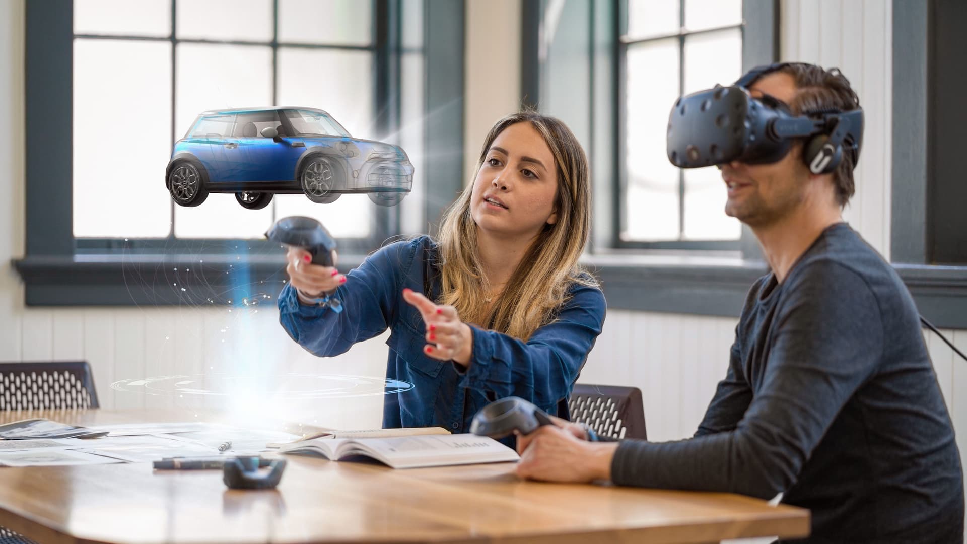 ### Welches Potenzial hat Virtual Reality für den deutschen Mittelstand? Mann mit VR Brille sitzt am Tisch. Neben ihm eine Frau die einen virtuellen Wagen beschreibt.
